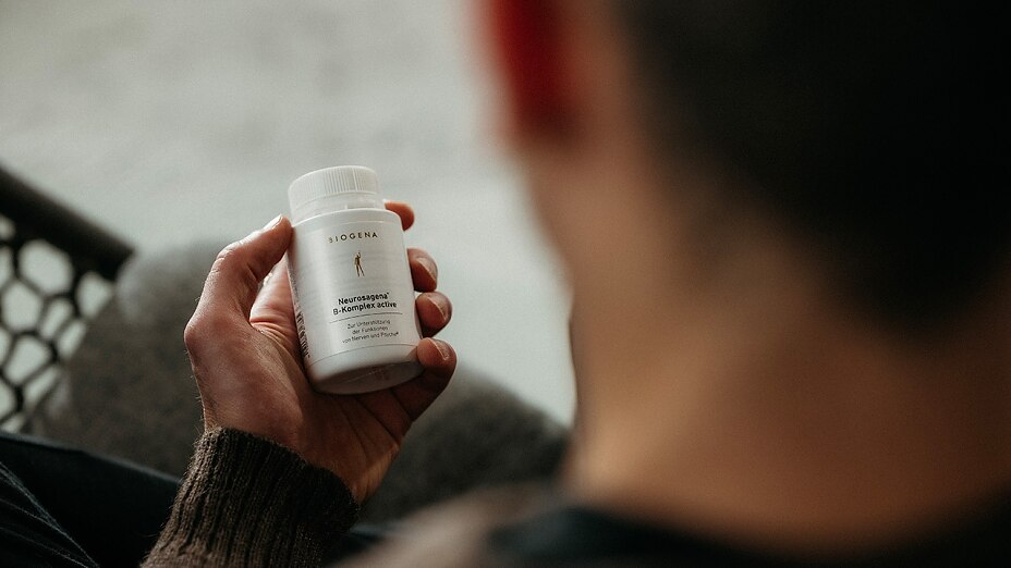 Mann hält Vitamin B Komplex Dose in der Hand und sieht sie an.