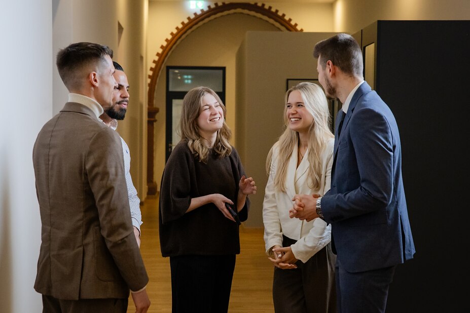 alt="Fünf Personen führen eine fröhliche Unterhaltung"