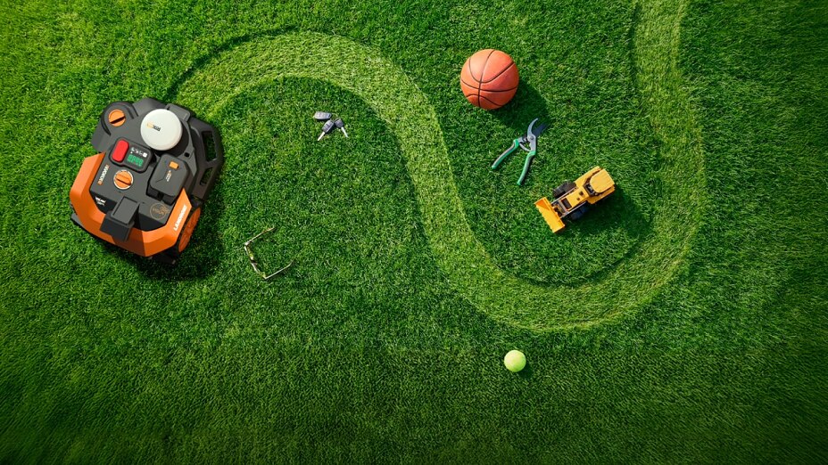 Draufsicht: WORX Landroid Mähroboter auf grünem Rasen, S-Kurven-Mähspur, meidet verstreute Alltagsgegenstände wie Bälle, Werkzeug und Spielzeug.