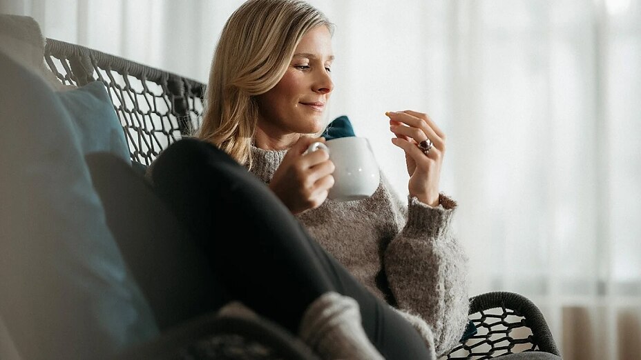 Entspannte Person sitzt auf bequemem Stuhl und nimmt Ashwagandha Kapsel ein