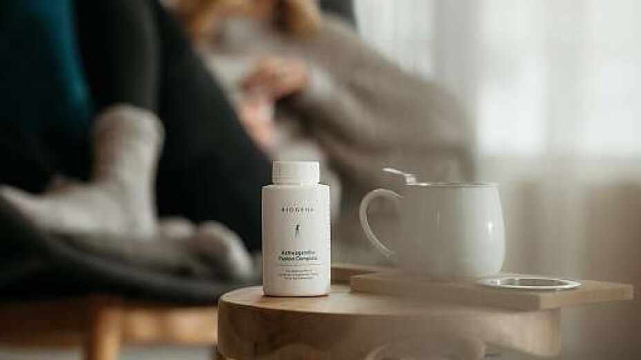 Supplement Dose BIOGENA Ashwagandha Fusion Complete steht auf Tisch neben weißer Tasse.