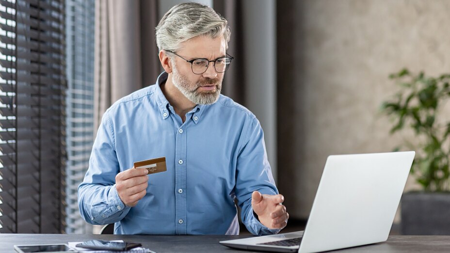 Mann mit Kreditkarte wird beim Online-Kauf auf seinem Laptop skeptisch