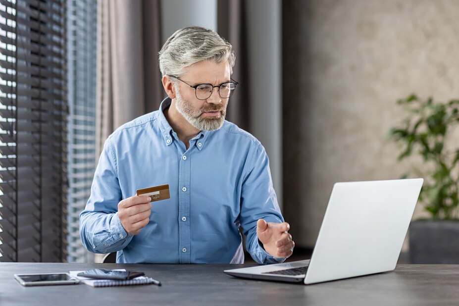 Mann mit Kreditkarte wird beim Online-Kauf auf seinem Laptop skeptisch