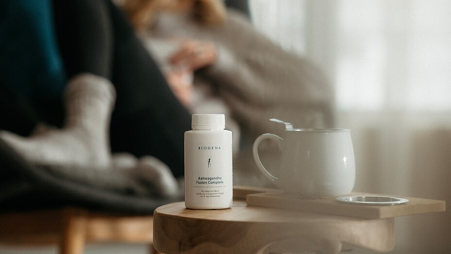 Supplement Dose BIOGENA Ashwagandha Fusion Complete steht auf Tisch neben weißer Tasse.