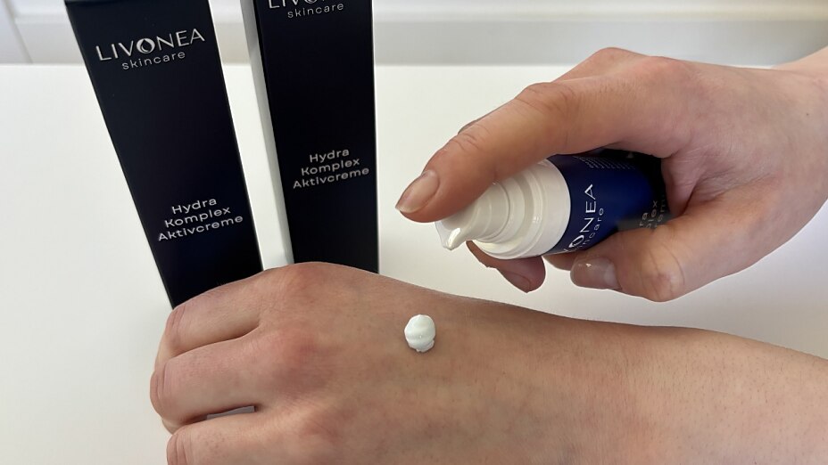 Anwendung der LIVONEA Hydra Komplex Aktivcreme: Eine Person dosiert einen Tropfen der weißen Creme aus dem Pumpspender auf ihren Handrücken.