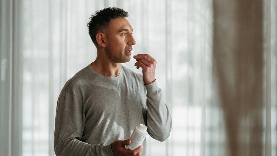 Person nimmt eine Kapsel ein und hält die BIOGENA Magnesiumbisgylcinat 125 Dose in der Hand.