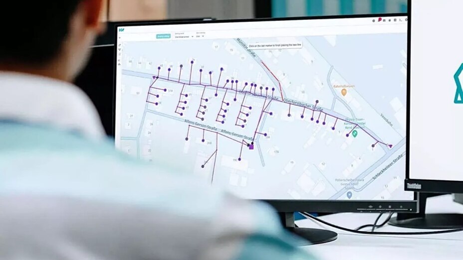 Mitarbeiter sitzt vor mehreren Bildschirmen und betrachtet eine digitale Darstellung eines Stromverteilnetzes in der Intelligent Grid Platform von envelio.