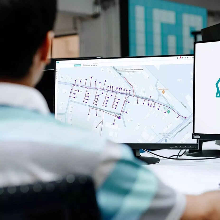 Mitarbeiter sitzt vor mehreren Bildschirmen und betrachtet eine digitale Darstellung eines Stromverteilnetzes in der Intelligent Grid Platform von envelio.