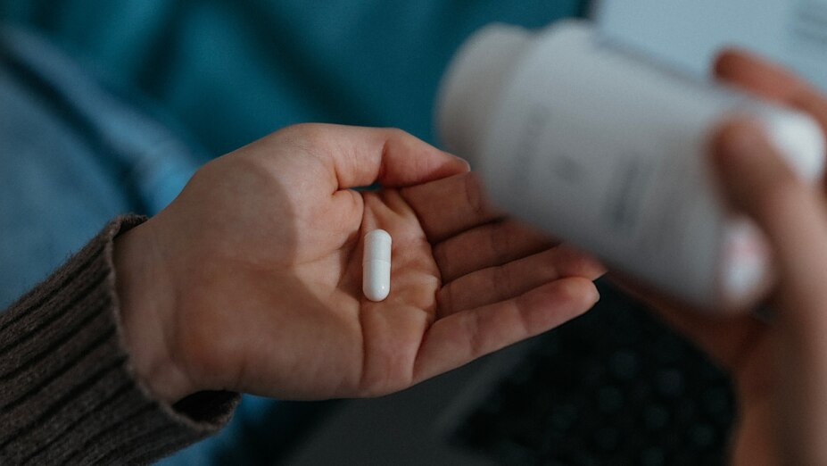 Eine Person kippt eine weiße Kapsel aus der BIOGENA Magnesiumbisglycinat 125 Dose in die geöffnete Hand.