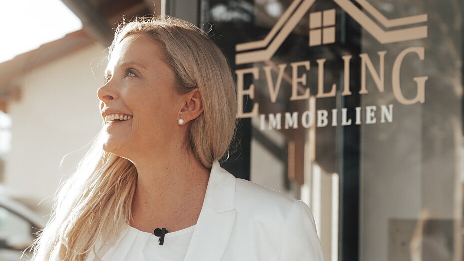 Das Bild zeigt Andrea Gabrisch, Immobilienmaklerin, Inhaberin und Geschäftsführerin von Eveling Immobilien, vor dem Eingang zu ihrem Büro in Grasbrunn.