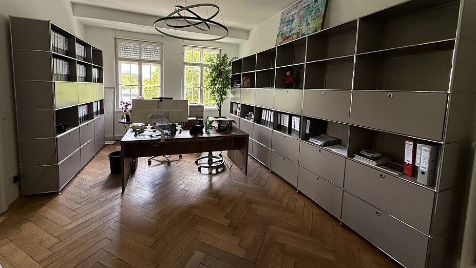 Büro mit modularen Flexcube Regalsystemen entlang zweier Wände, Schreibtisch und Parkettboden