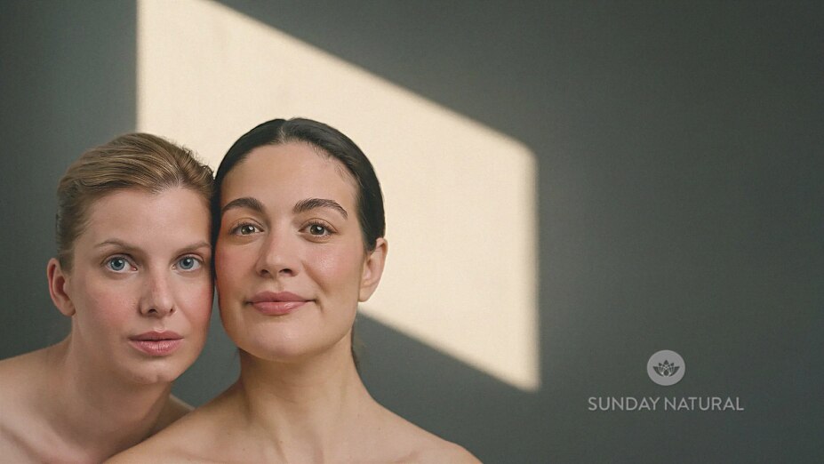 Zwei Frauen mit natürlicher Ausstrahlung blicken selbstbewusst in die Kamera, beleuchtet von warmem Sonnenlicht. Unten rechts ist das Logo von Sunday Natural zu sehen.