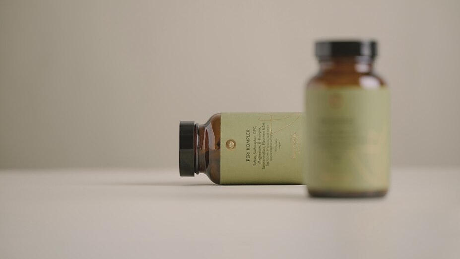 Zwei Braunglasflaschen mit grünem Etikett von Sunday Natural stehen auf einer hellen Oberfläche. Die liegende Flasche im Fokus trägt die Aufschrift "Peri Komplex".